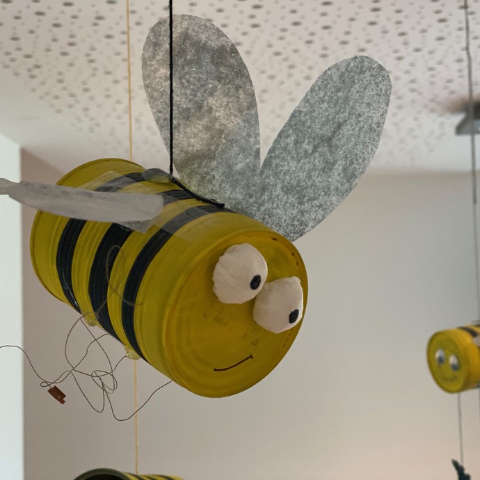 Zwei schwarzgelb bemalte Dosen, mit einem Gesicht und Flügeln versehen stellen fliegende Bienen vor (vergrößerte Bildansicht wird geöffnet)