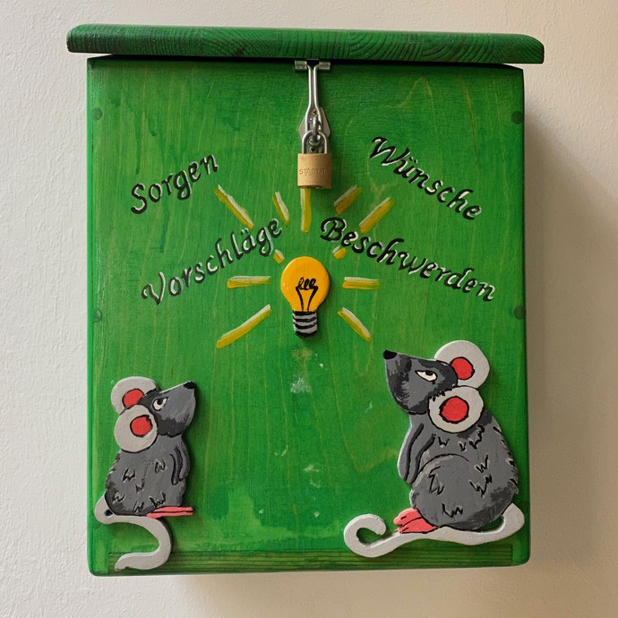 Ein grüner Briefkasten mit der Aufschrift "Sorgen, Beschwerden" in der  Mitte eine gemalte Glühbirne, darunter zwei gemalte Mäuse (öffnet vergrößerte Bildansicht)