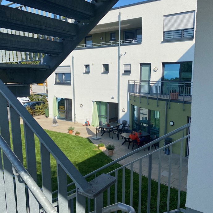 Blick von oben auf eine sonnenbeschinene Terrasse mit Stühlen und Tischen. An einem Tisch sitzt ein Mann (vergrößerte Bildansicht wird geöffnet)