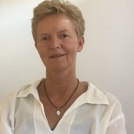 Ein Frau mit modernem Kurzhaarschnitt trägt eine weiße Bluse. Sie lächelt interessiert in die Kamera
