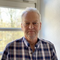 Ein Mann mit kurzen grauen Haaren trägt ein kariertes Hemd und schaut interessiert in die Kamera Ein Mann mit kurzen grauen Haaren trägt ein kariertes Hemd und schaut interessiert in die Kamera