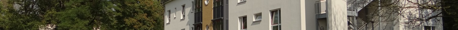 Sonnenbeschienene Gartenansicht der Fassade des Wolfgang-Leonhardt-Hauses auf dem LWL-Klinikgelände. Im Vordergrund hölzerne Sitzgelegenheiten