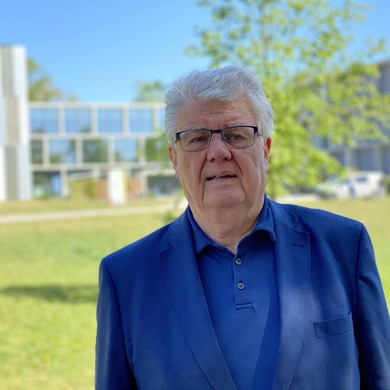 Ein Mann in blauem Sakko steht vor einem modernen Gebäude und schaut interessiert in die Kamera Ein Mann in blauem Sakko steht vor einem modernen Gebäude und schaut interessiert in die Kamera